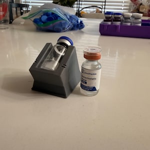 Könnte beinhalten: Eine klare Glasflasche mit orangefarbenem Verschluss und der Aufschrift "CloudPeptide Bacteriostatic Water". Eine zweite Flasche wird in einem grauen Ständer gehalten. Zusätzliche blaue Kappen sind im Hintergrund zu sehen.