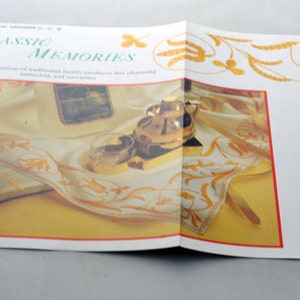 May include: A brochure titled "Classic Memories" showcasing a white tablecloth with gold embroidery. The embroidery features a floral design with leaves and flowers. The brochure also includes a photograph of a book and a decorative metal object.