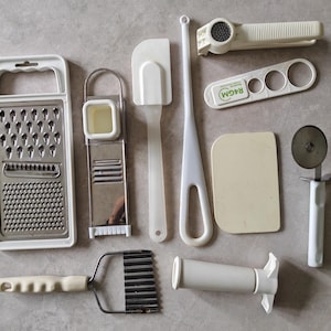 May include: A collection of kitchen tools including a grater, a garlic press, a pizza cutter, a spatula, a pastry scraper, a cookie cutter, a measuring tool, and a pastry brush.