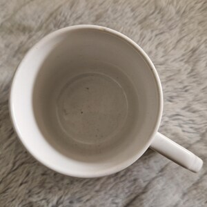 May include: White ceramic mug with a smooth, slightly textured surface. The mug is empty and has a handle.