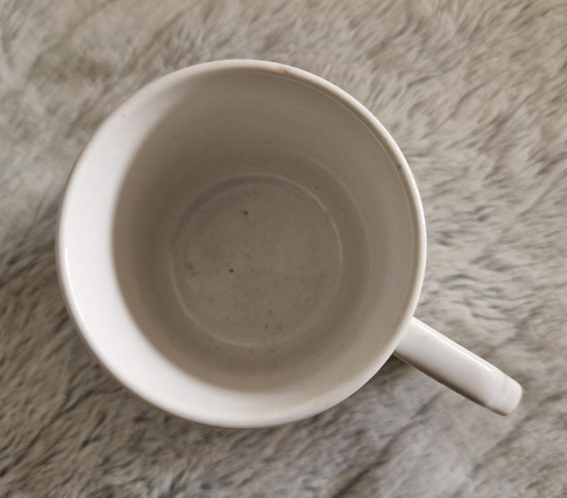 May include: White ceramic mug with a smooth, slightly textured surface. The mug is empty and has a handle.
