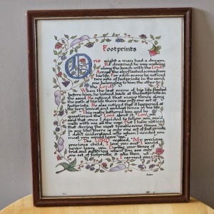 May include: A framed print of the poem "Footprints", with a decorative floral border and grape vine accents. The text is in an elegant script. The frame is a dark brown colour.