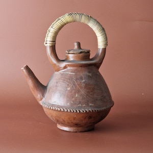 May include: A brown clay teapot with a woven handle and intricate etched designs. The teapot has a rounded body and a small spout.