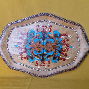 May include: A wooden tray featuring a decorative design painted in blue, red, and white. The design incorporates a floral pattern with a central motif.
