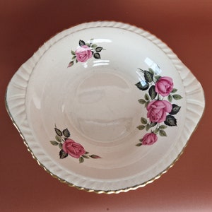 May include: A white ceramic bowl with a gold rim and a floral design featuring pink roses and green leaves.