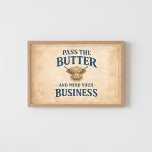 May include: A framed print with the text "PASS THE BUTTER" above "-AND MIND YOUR- BUSINESS". The artwork features a watercolor illustration of a Highland cow. The background has a parchment paper texture.