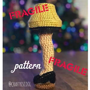 May include: A crocheted lampshade with a yellow base and a black rim, shaped like a leg wearing fishnet stockings and black shoes. The lampshade is labeled "FRAGILE" in red letters. The text "pattern" and "@CRAFTYISCOOL" are also visible.