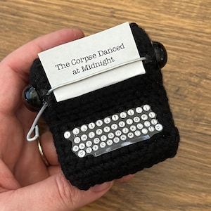 May include: Black crocheted typewriter with a white label that reads "The Corpse Danced at Midnight".