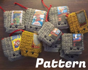 May include: A collection of crocheted Nintendo game cartridge pouches in gray and yellow with various game titles including Super Mario 2, Duck Hunt, Zelda, and Castlevania. The pouches have cute faces with black eyes and red yarn for mouths.