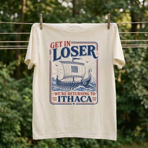 Puede incluir: Una camiseta de manga corta color crema con un gr&aacute;fico azul y rojo de un barco antiguo en el oc&eacute;ano. El texto dice GET IN LOSER WE'RE RETURNING TO ITHACA. El dise&ntilde;o est&aacute; encerrado en un borde rectangular con l&iacute;neas decorativas y estrellas.