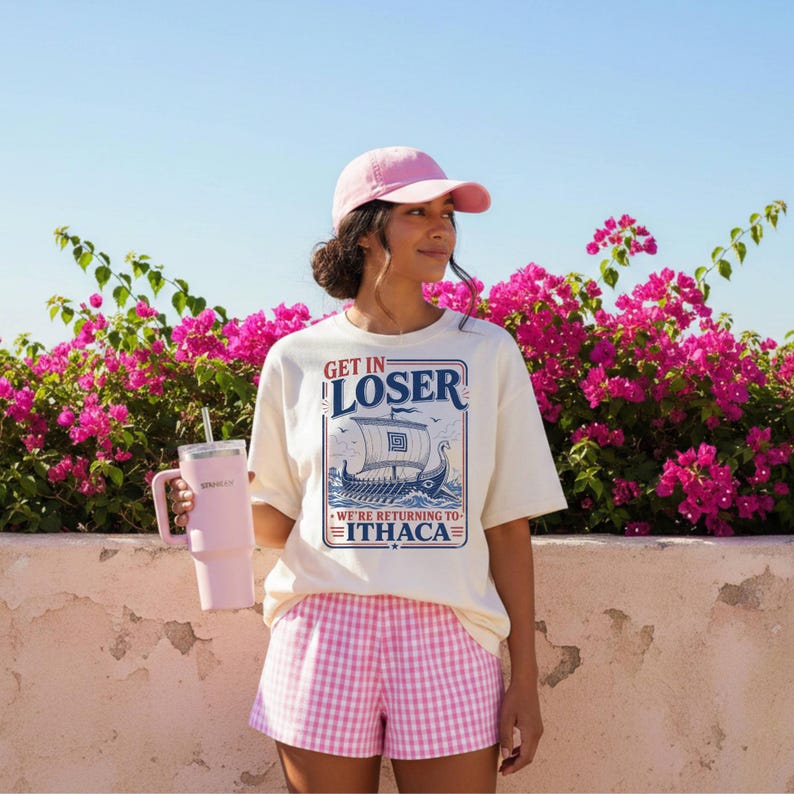 Puede incluir: Una camiseta de color claro con un gr&aacute;fico de un barco y el texto "GET IN LOSER WE'RE RETURNING TO ITHACA", combinada con pantalones cortos de cuadros vichy rosas, una gorra de b&eacute;isbol rosa claro y un vaso t&eacute;rmico rosa claro con pajita.