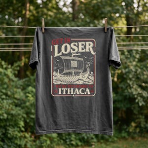 Puede incluir: Una camiseta gris carb&oacute;n de manga corta con un estampado gr&aacute;fico de un antiguo barco griego en el mar. El texto dice GET IN LOSER WE'RE RETURNING TO ITHACA en letras color crema y rojo, enmarcado por un borde rectangular en la parte frontal.