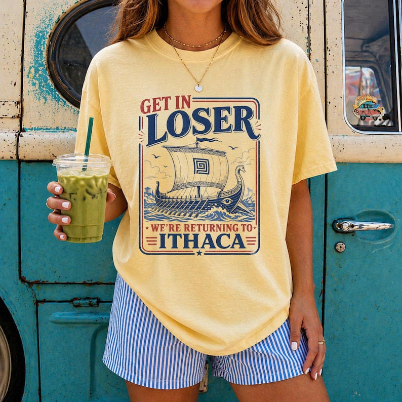 Puede incluir: Una camiseta de manga corta de color amarillo p&aacute;lido con un gr&aacute;fico de un barco trirreme griego en el oc&eacute;ano. El texto dice GET IN LOSER WE'RE RETURNING TO ITHACA. El dise&ntilde;o est&aacute; enmarcado en un borde rectangular con detalles en azul y rojo.