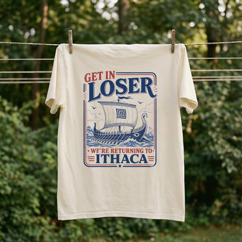 Puede incluir: Una camiseta de manga corta color crema con un gr&aacute;fico azul y rojo de un barco antiguo en el oc&eacute;ano. El texto dice GET IN LOSER WE'RE RETURNING TO ITHACA. El dise&ntilde;o est&aacute; encerrado en un borde rectangular con l&iacute;neas decorativas y estrellas.