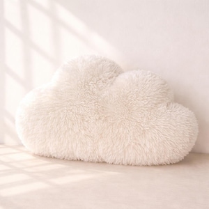 May include: A soft, white cloud-shaped cushion. The cushion has a fluffy, textured surface, designed to resemble a cloud. It is a decorative item, suitable for a bedroom or living room.