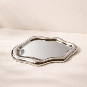 May include: A polished, silver-colored tray with an organic, cloud-like shape. The tray has a reflective surface and a smooth, rounded edge. This decorative tray is suitable for serving or display.