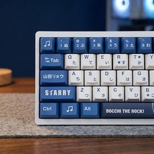May include: A close-up of a white and blue mechanical keyboard. The keyboard has blue keycaps with white lettering and Japanese characters. The bottom row of keys reads "BOCCHI THE ROCK!" and "STARRY".
