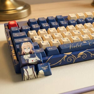 Könnte beinhalten: Eine individuelle mechanische Tastatur mit blauen und cremefarbenen Tastenkappen. Die Tastatur hat eine blaue Basis mit goldenen floralen Akzenten und dem Wort "Violet" in Schreibschrift. Einige Tastenkappen zeigen Anime-Charaktere.