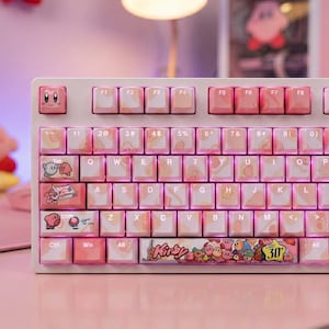 May include: A pink and white mechanical keyboard with custom keycaps. The keyboard has pink and peach-coloured keys, with custom designs and the word "Kirby" on the spacebar. The number "30" is also visible.