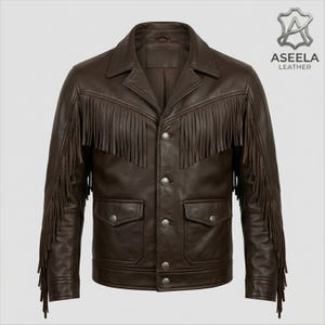 Peut inclure: Veste en cuir marron avec des franges décoratives sur la poitrine et les manches. La veste a une fermeture boutonnée, deux poches avant et un col classique. Le logo "ASEELA LEATHER" est visible en haut à droite.