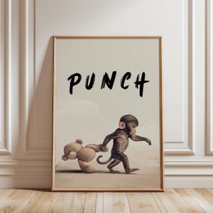 Könnte beinhalten: Ein gerahmter Druck zeigt einen Affen, der einen Teddybären zieht. Das Wort "PUNCH" steht in Schwarz über dem Affen. Das Kunstwerk hat eine neutrale Farbpalette und ist vor einem hellbeigen Hintergrund platziert.