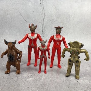 May include: A collection of five plastic action figures including a brown horned monster, two red and silver humanoid figures with pointed head designs, a smaller red and silver humanoid figure, and a gold mechanical robot with square chest details.