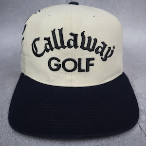 Op de afbeelding: Een baseballpet met een crèmekleurig voorpaneel en de zwarte geborduurde tekst Callaway GOLF. De pet heeft een effen zwarte klep en een achterpaneel van mesh, met een kleine zwarte knoop bovenop het midden van de kroonstructuur.