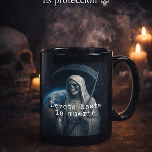 Puede incluir: Taza de cerámica negra con un diseño de la Parca con una guadaña y el texto "Devoto hasta la muerte". La taza también tiene el texto "NO ES SOLO UNA TAZA... Es protección" y un gráfico de calavera. Velas y una calavera en el fondo.