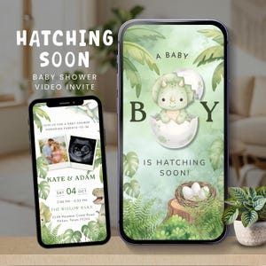May include: Two smartphones displaying a digital baby shower video invitation with a dinosaur theme. The screens feature a green watercolour background with palm leaves, a baby triceratops hatching from an egg, and text reading A BABY BOY IS HATCHING SOON, KATE & ADAM, and event details.