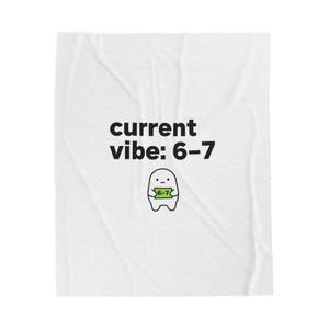 May include: White blanket with the text "current vibe: 6-7" in black. Below the text is a small cartoon character holding a green sign that reads "6-7". The blanket has a slightly wrinkled texture.