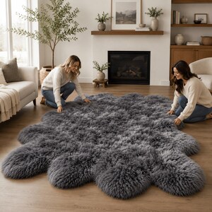 May include: A large, dark gray, circular area rug with a thick, shaggy, faux fur texture. The rug features a distinct scalloped or petal-like edge design, creating a soft, plush appearance that covers a significant portion of the wooden floor.