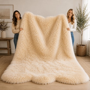 May include: A large, rectangular, cream-colored faux fur rug with a thick, shaggy pile texture. The rug features a soft, dense appearance with long, wavy fibers that create a plush surface. The edges of the rug have a rounded, organic shape.
