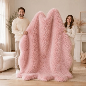 May include: A large, irregularly shaped rug made of long, soft, pink faux fur. The rug features a dense, shaggy texture with a consistent light pink color throughout its entire surface, showcasing a natural, organic outline with curved edges.