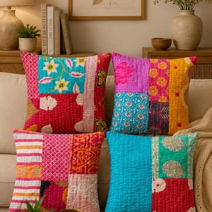 May include: Four colorful patchwork throw pillows with floral and geometric patterns. The pillows are arranged on a beige sofa, showcasing a variety of colors including red, blue, pink, and orange. The pillows add a decorative touch to the living room.