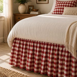 Peut inclure: Un cache-sommier à motif vichy rouge et blanc. Le tissu est froncé pour créer un effet volanté le long de la base du lit, qui est recouvert d'une couette couleur crème unie et d'un oreiller assorti à carreaux rouges et blancs.