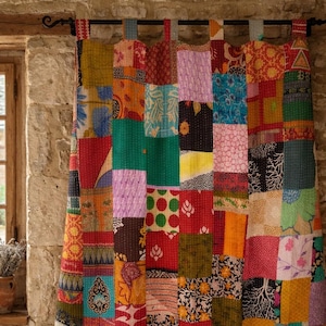 Puede incluir: Una cortina de patchwork hecha de cuadrados de tela de varios colores vibrantes como rojo, verde y naranja. La cortina cuelga frente a una pared de piedra, con una ventana y una pequeña maceta con flores secas visibles.