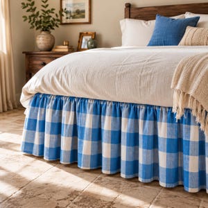 May include: A bed skirt featuring a blue and white buffalo check pattern with a gathered, ruffled design. The fabric is draped around the base of the bed, extending from the bottom of the mattress to the floor, creating a decorative border.