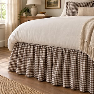 May include: A bed skirt featuring a brown and white gingham check pattern with a gathered, ruffled design. The bed skirt is positioned beneath a white duvet cover, with matching brown and white gingham pillow shams visible at the head of the bed.