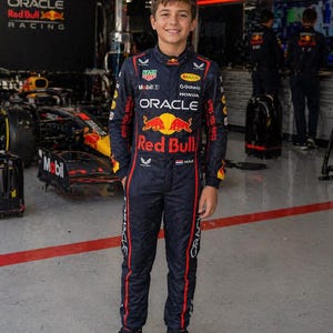 Op de afbeelding: Een donkerblauw racepak met rode en gele accenten, voorzien van diverse sponsorlogo's waaronder Oracle, Red Bull, Honda en Mobil. Het pak toont de tekst Red Bull, Oracle en Max, samen met een kleine Nederlandse vlag op de borstzijde.