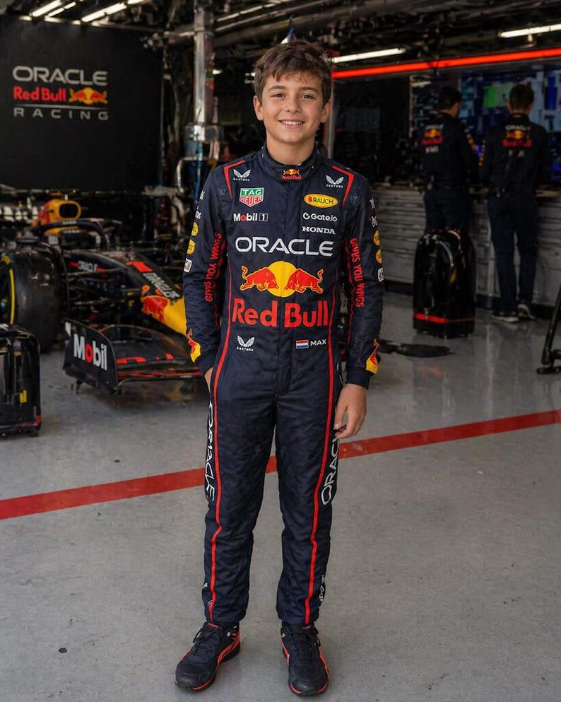 Op de afbeelding: Een donkerblauw racepak met rode en gele accenten, voorzien van diverse sponsorlogo's waaronder Oracle, Red Bull, Honda en Mobil. Het pak toont de tekst Red Bull, Oracle en Max, samen met een kleine Nederlandse vlag op de borstzijde.