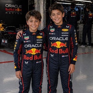 Op de afbeelding: Twee personen in bijpassende donkerblauwe Oracle Red Bull Racing team-overalls met rode en gele sponsorlogo's, waaronder Oracle, Red Bull, Honda en Tag Heuer, met een kleine Nederlandse vlag en de naam Max op de borst.
