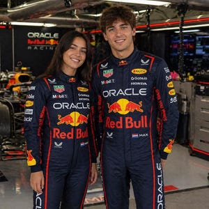 Op de afbeelding: Een donkerblauwe Oracle Red Bull Racing team-overall met rode en gele accenten, voorzien van sponsorlogo's zoals Tag Heuer, Mobil 1, Honda en Oracle op de borst, mouwen en benen, gedragen door twee personen in een garageomgeving.