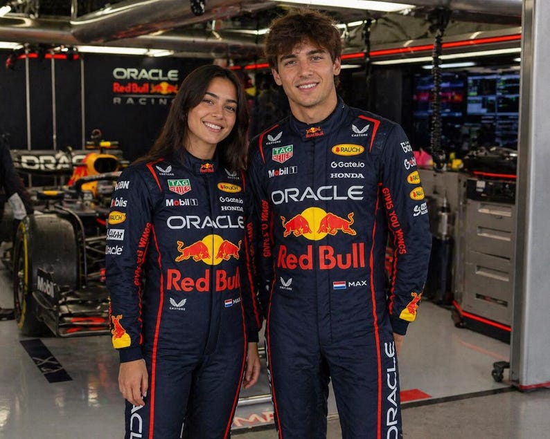 Op de afbeelding: Een donkerblauwe Oracle Red Bull Racing team-overall met rode en gele accenten, voorzien van sponsorlogo's zoals Tag Heuer, Mobil 1, Honda en Oracle op de borst, mouwen en benen, gedragen door twee personen in een garageomgeving.