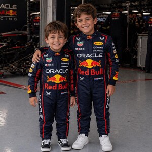Op de afbeelding: Twee donkerblauwe race-overalls met het Oracle Red Bull Racing-logo, de rode stier-afbeelding en diverse sponsorpatches zoals TAG Heuer, Mobil 1 en Honda. De overalls hebben rode biezen langs de zijkanten en een klein Nederlands vlaggetje.
