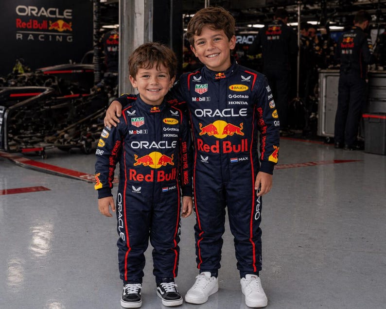 Op de afbeelding: Twee donkerblauwe race-overalls met het Oracle Red Bull Racing-logo, de rode stier-afbeelding en diverse sponsorpatches zoals TAG Heuer, Mobil 1 en Honda. De overalls hebben rode biezen langs de zijkanten en een klein Nederlands vlaggetje.