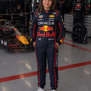 Op de afbeelding: Een donkerblauwe raceoverall van het Oracle Red Bull Racing-team met rode en gele sponsorlogo's, waaronder Oracle, Red Bull, Mobil 1 en Honda. Het pak heeft een hoge kraag, lange mouwen en een Nederlandse vlag met de naam MAX op de borst.