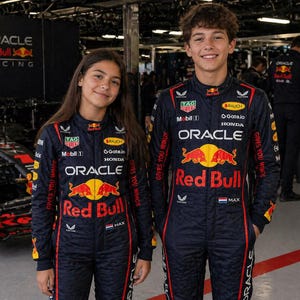 Op de afbeelding: Twee personen in donkerblauwe Oracle Red Bull Racing raceoveralls met rode en gele sponsorlogo's, waaronder Oracle, Red Bull, Honda en Tag Heuer, de tekst Gives You Wings en een kleine Nederlandse vlag op de borst.
