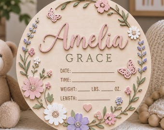 May include: A circular wooden birth announcement sign featuring the name Amelia Grace in raised pink and dark lettering. The board includes fields for date, time, weight in lbs and oz, and length, decorated with painted flowers and butterflies.