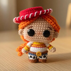 May include: Crocheted doll of a character with orange hair, a red hat, and a white shirt with yellow stripes. The doll has black button eyes and blue jeans with a cow print. The doll is handmade.