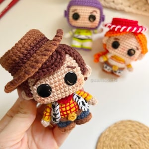 May include: Crocheted Toy Story character dolls, including Woody with a brown hat, Buzz Lightyear in a purple and green suit, and Jessie with a red hat. The dolls are handmade with detailed features and large black eyes.